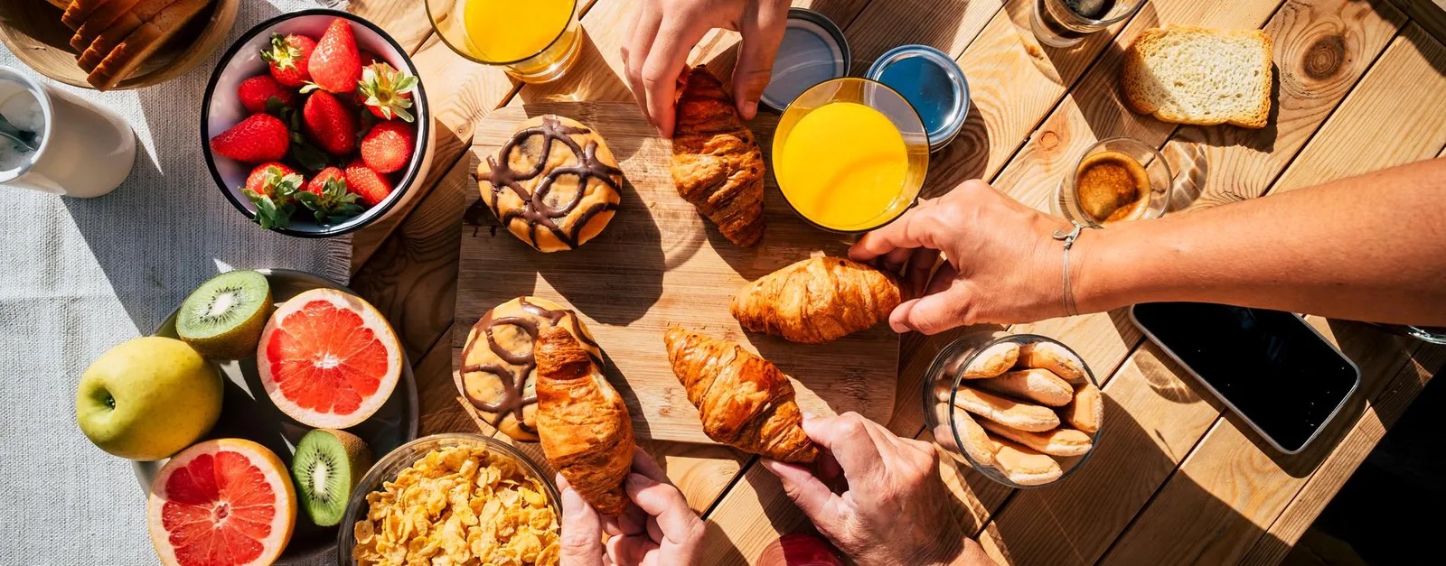 Mesa de desayuno servida con jugo de naranja, medialunas y fruta